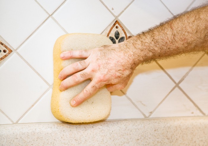 Worker’s hand using a sponge to wipe fresh grout from ceramic tile
